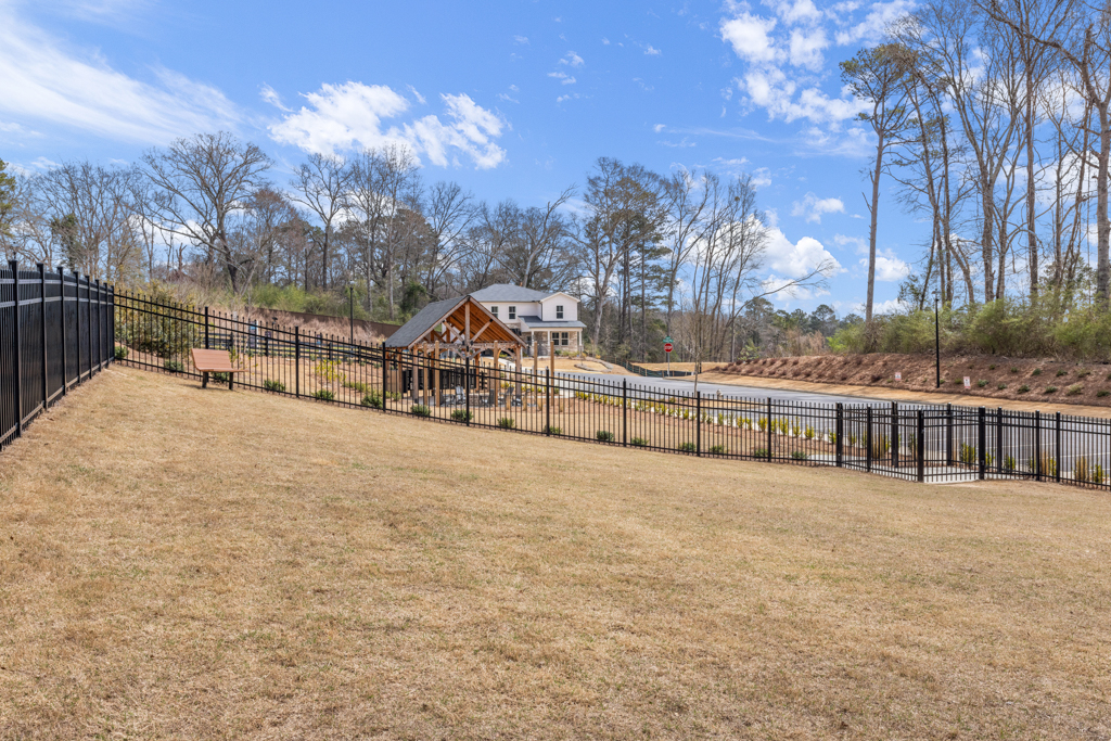A fenced in dirt field with a house in the background.